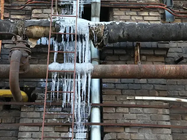Ice hanging from frozen supply pipes along a brick wall in winter