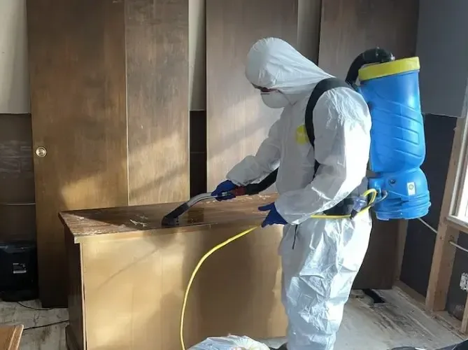 A technician in a full protective suit spraying antimicrobial on cabinets after a sewage backup