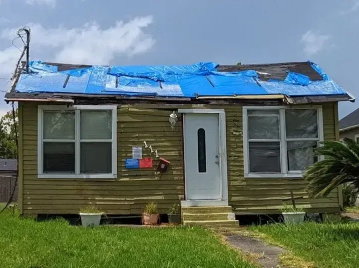 A small house with a blue tarp stretched over its storm-damaged roof