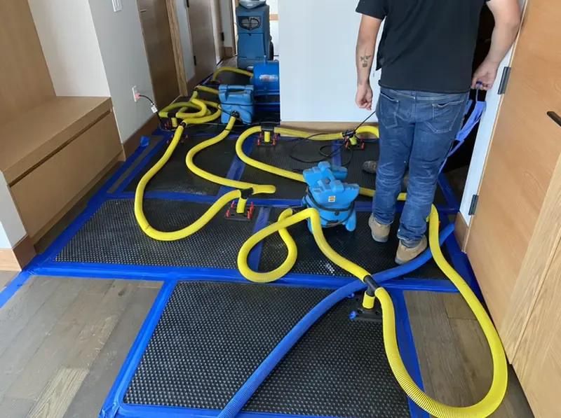 Drying mats on a hardwood floor linked by yellow hoses during structural drying